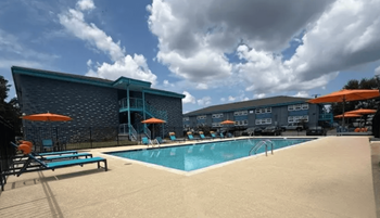 A swimming pool area with sun loungers and umbrellas in front of a building.